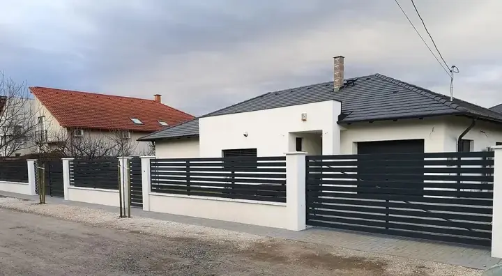 Antracit vízszintes lemezléc kerítés fehér vakolt pillérekkel modern családi ház előtt